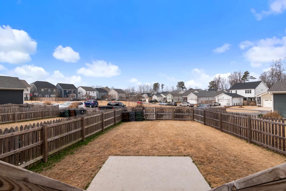 Back gardens in a new-build neighbourhood, each enclosed by a wood privacy fence, under a clear sky.